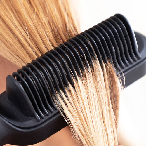 Gros plan sur les picots en céramique noire de la brosse lissante glissant dans une mèche de cheveux blonds