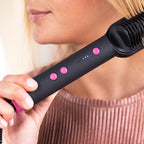 Gros plan sur le manche noir de la brosse lissante et ses boutons roses (marche, plus, moins) avec les témoins de température allumés