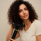 Femme aux cheveux bouclés tenant l'appareil muni de son diffuseur noir, t-shirt écru, fond beige